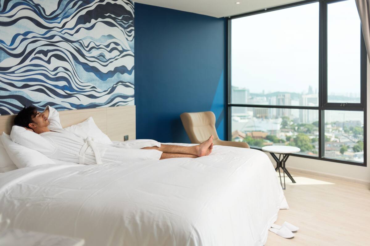 Ein modernes Hotelzimmer mit einem großen Bett, Blick auf die Stadt und einer blauen Akzentwand.