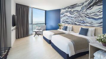 A modern hotel room with two beds, a large window, a flat-screen TV, and a view of the city.