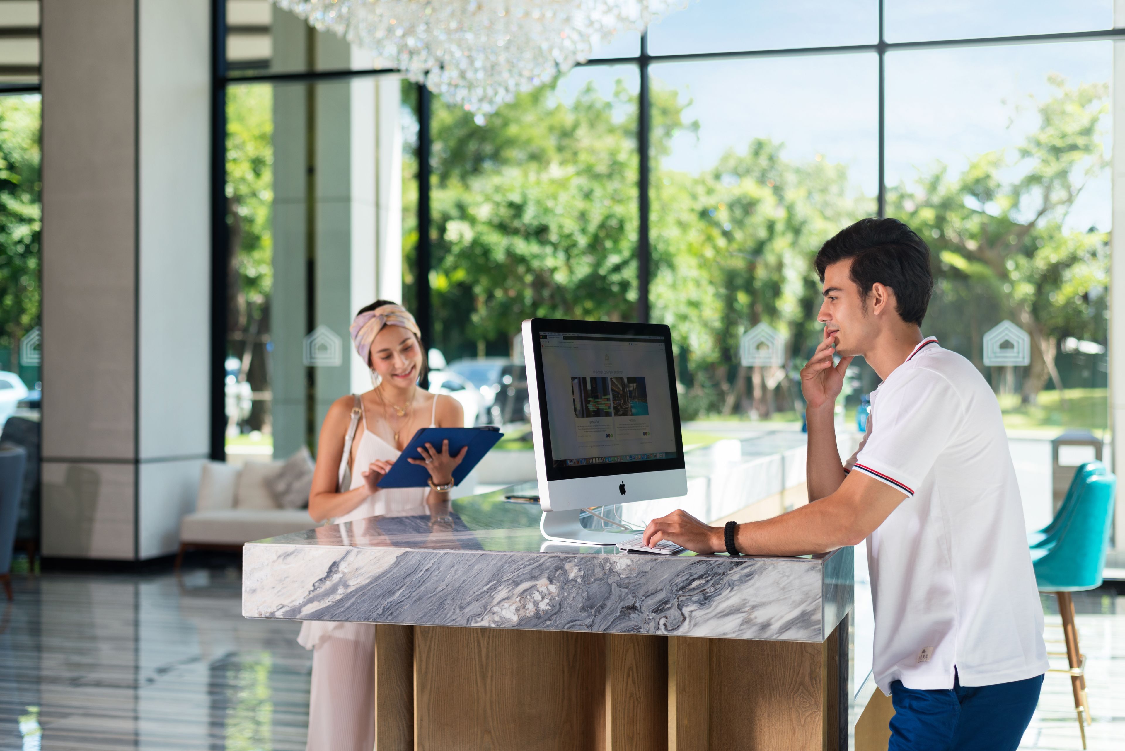 A reception desk with a large monitor, a woman holding a tablet, and a man standing beside it.