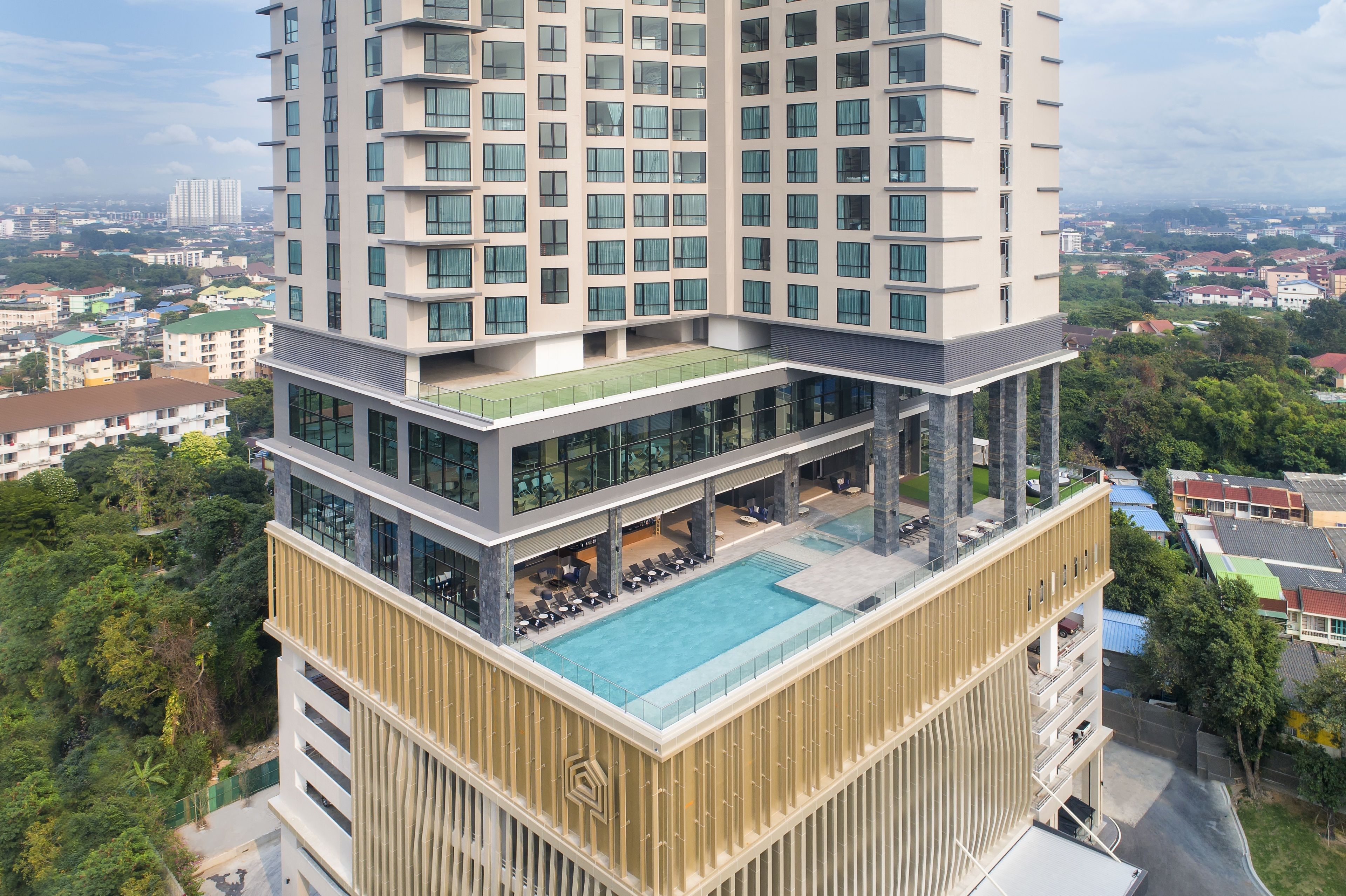 A high-rise hotel with multiple floors, a rooftop pool, and a lush green surrounding.
