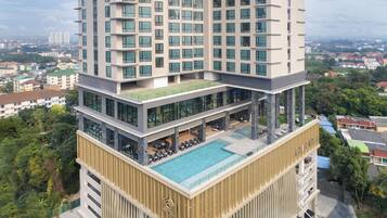 A high-rise hotel with multiple floors, a rooftop pool, and a lush green surrounding.