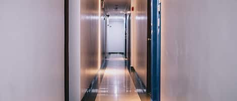 A long, narrow hallway with a shiny tiled floor, a blue door on the right, and a light fixture on the left.