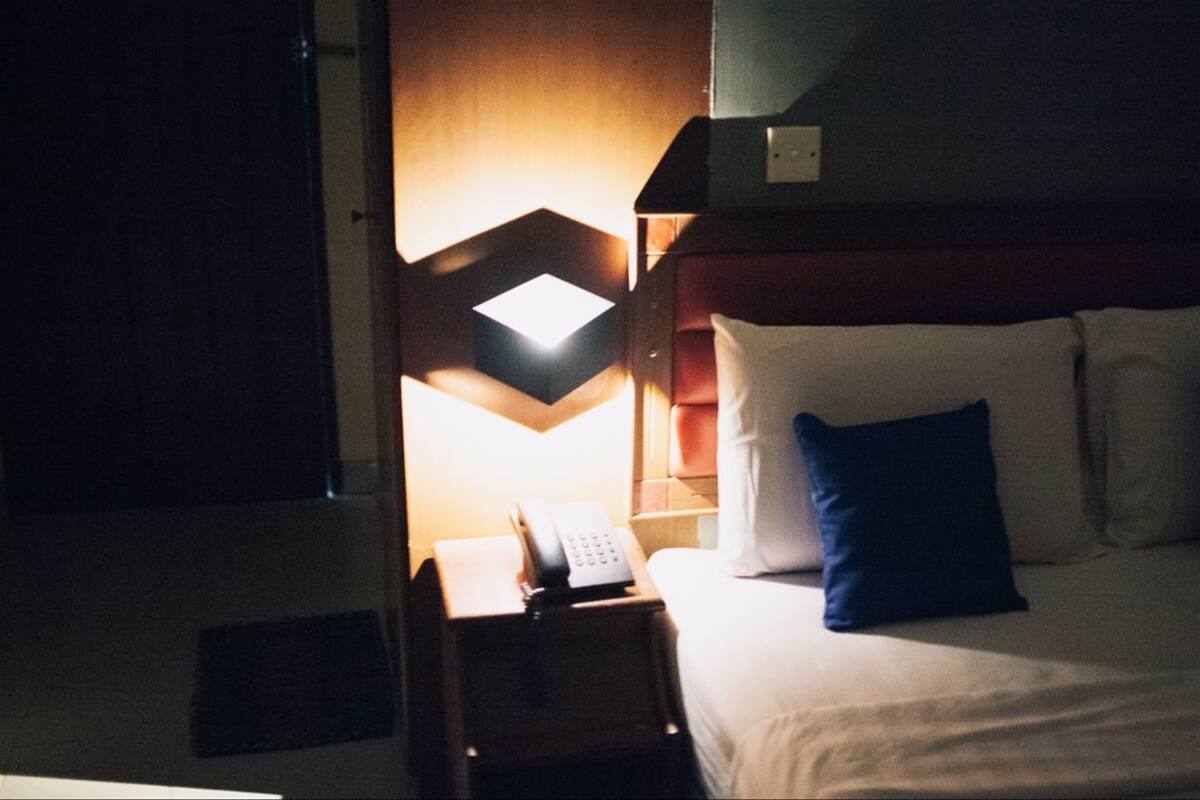 A hotel room with a bed, a nightstand with a phone, and a wall-mounted light fixture.