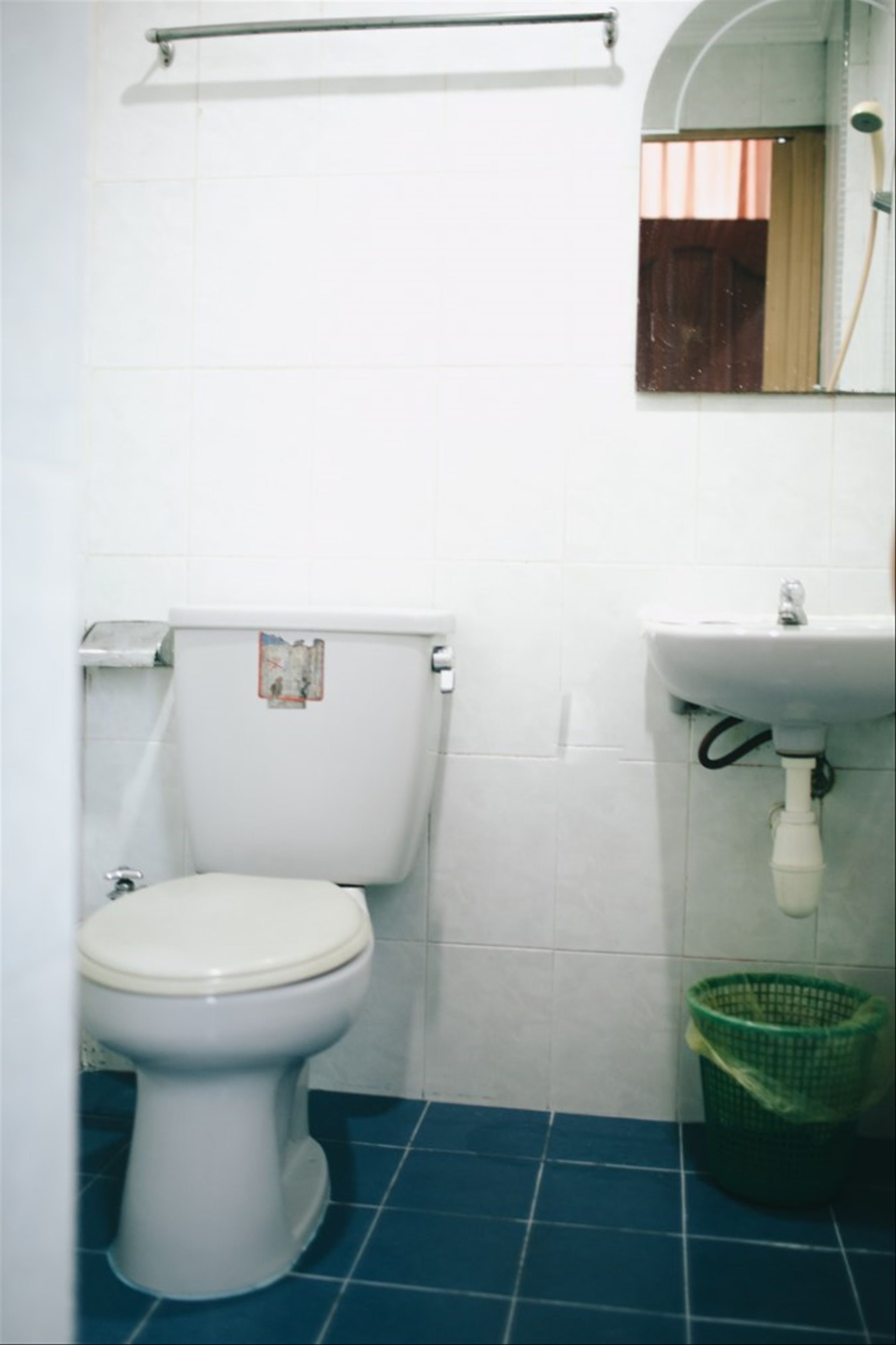A small bathroom with a toilet, a sink, and a green trash bin.