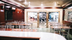 Un restaurante con varias mesas y sillas, interior de madera y amplios ventanales con paneles de vidrio decorativos.