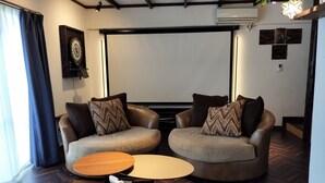 Uma sala de estar moderna com duas poltronas de couro, uma mesa de centro de madeira e uma tela grande para visualização.