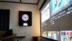 Uma sala de estar com um alvo de dardos, uma televisão exibindo conteúdo japonês e um sofá.