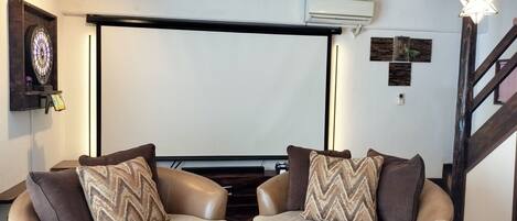 A cozy living room with two leather armchairs, a small table, and a projector screen.