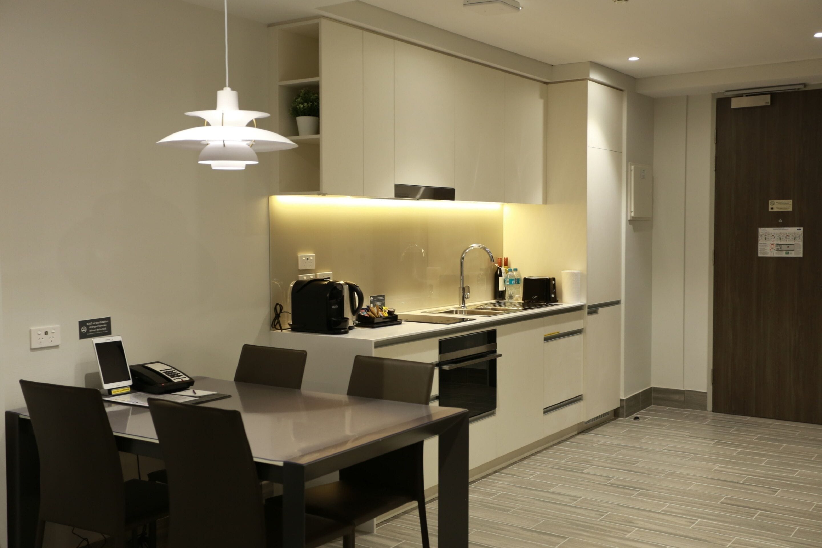 A modern kitchen with a dining area, white cabinets, a built-in oven, and a coffee machine.