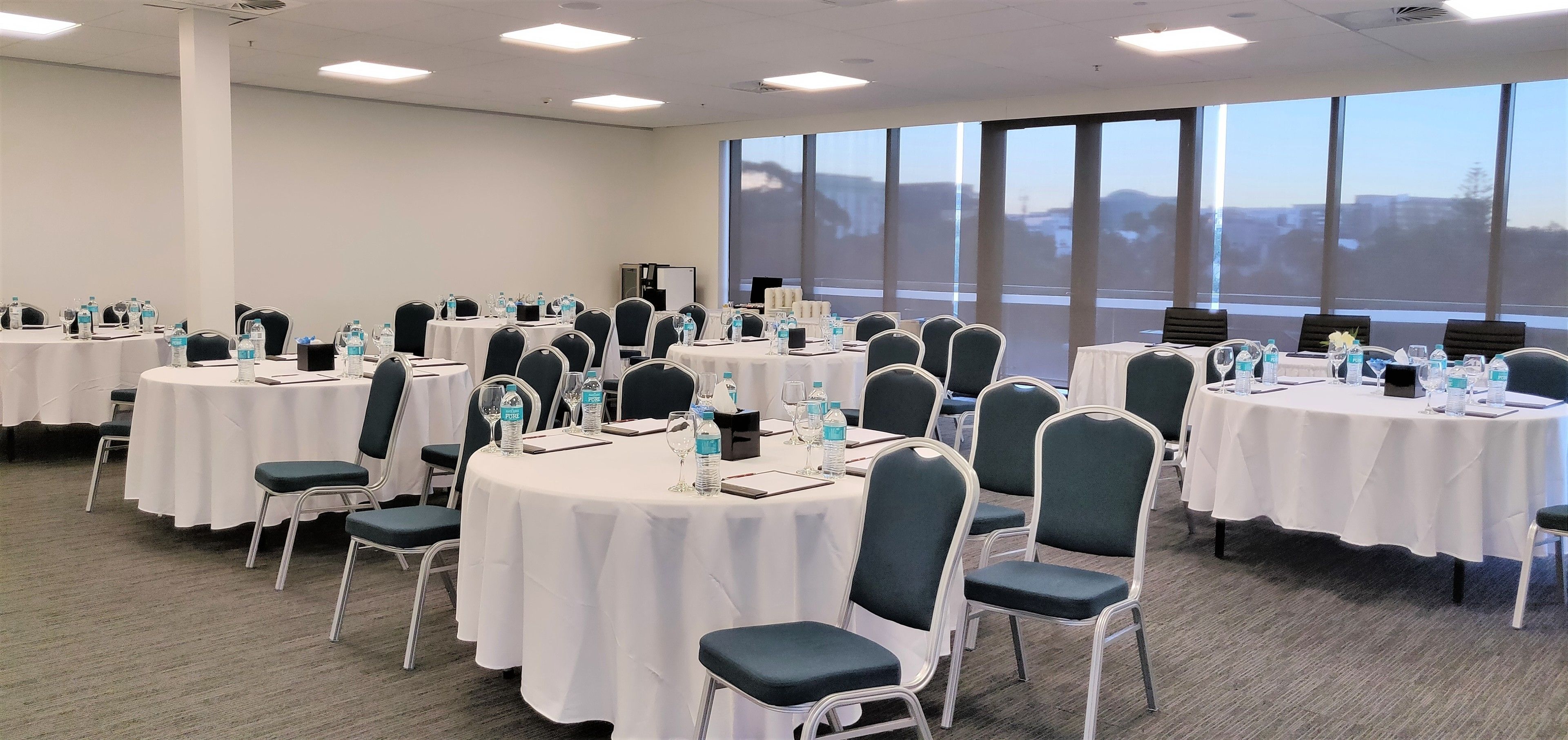 Un salón de conferencias con varias mesas redondas, cada una con sillas, botellas de agua y tarjetas de identificación.