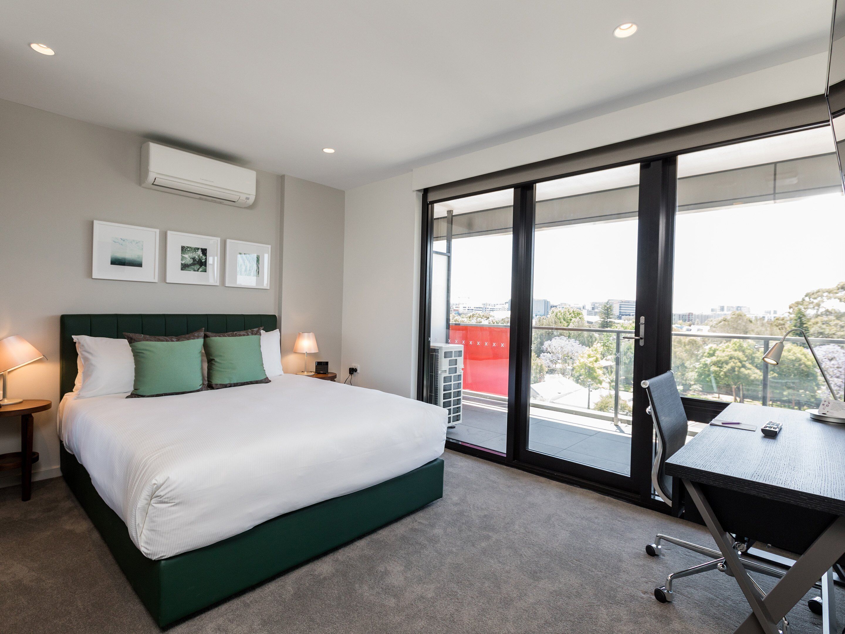 A modern hotel room with a large bed, a desk, and a view of the city through large windows.