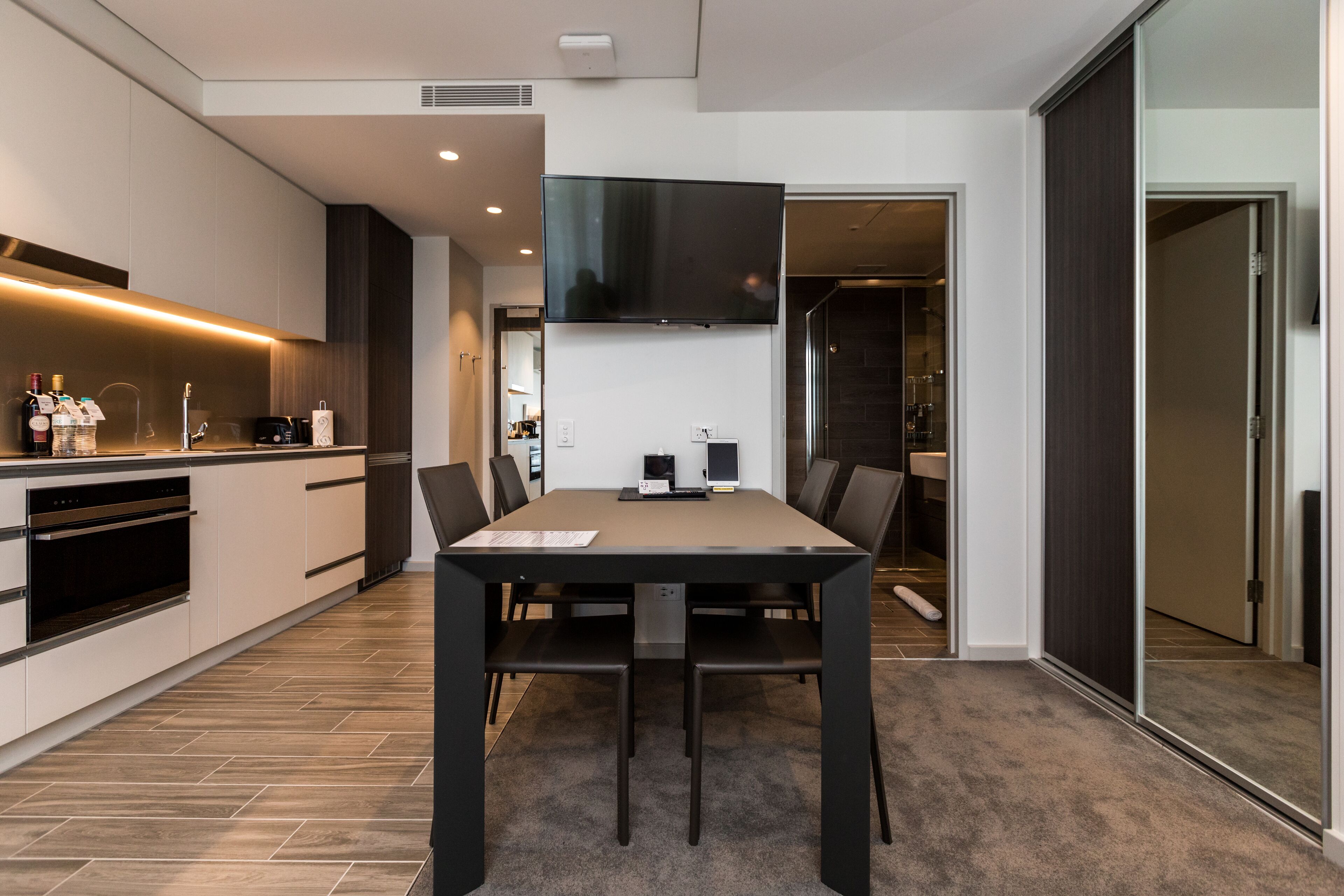 A modern kitchen with a dining area, built-in appliances, and a flat-screen TV.