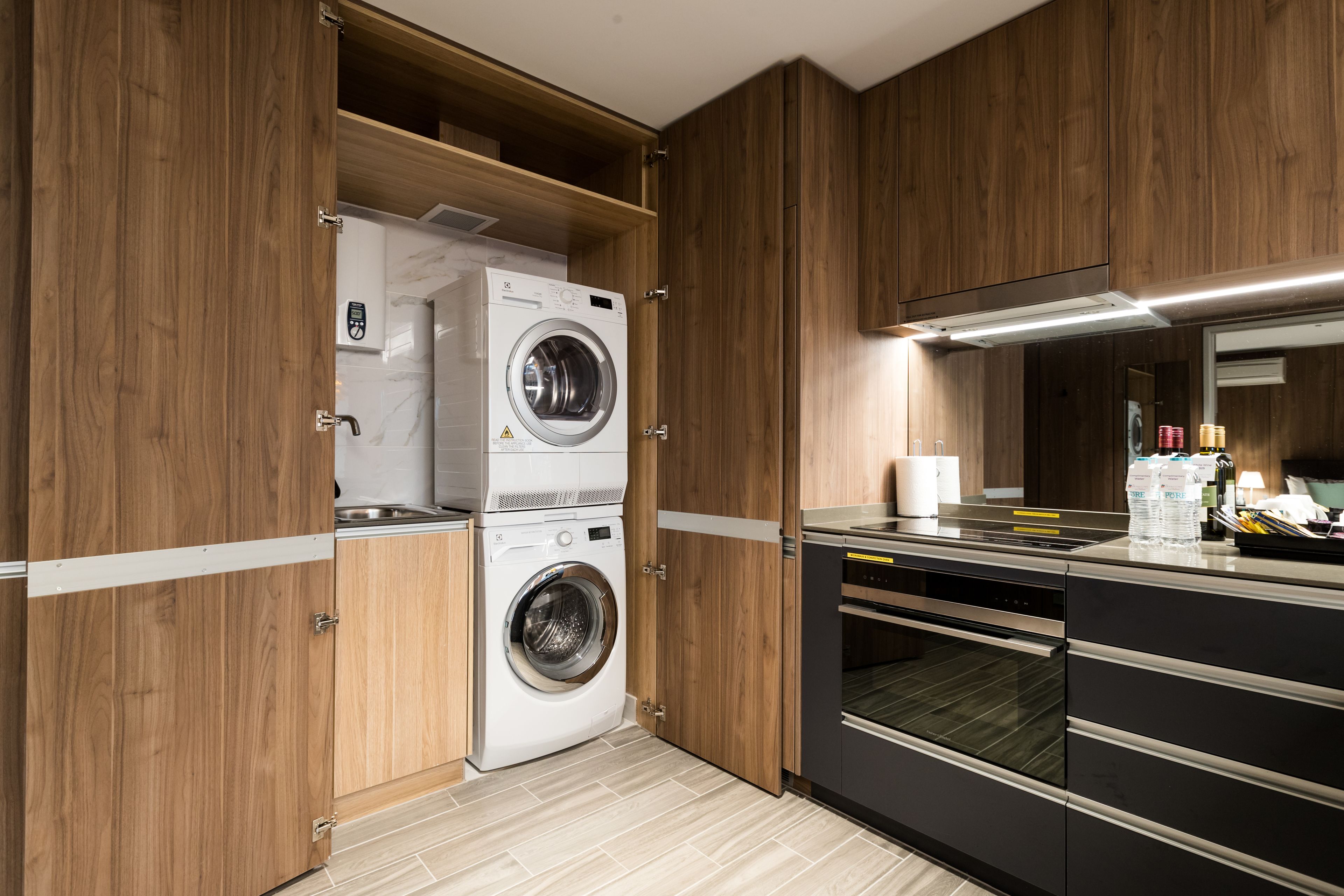A modern kitchen with wooden cabinets, a built-in washer and dryer, and a stainless steel countertop.