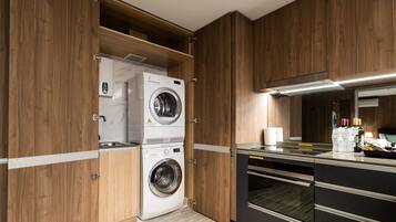 A modern kitchen with wooden cabinets, a built-in washer and dryer, and a stainless steel countertop.
