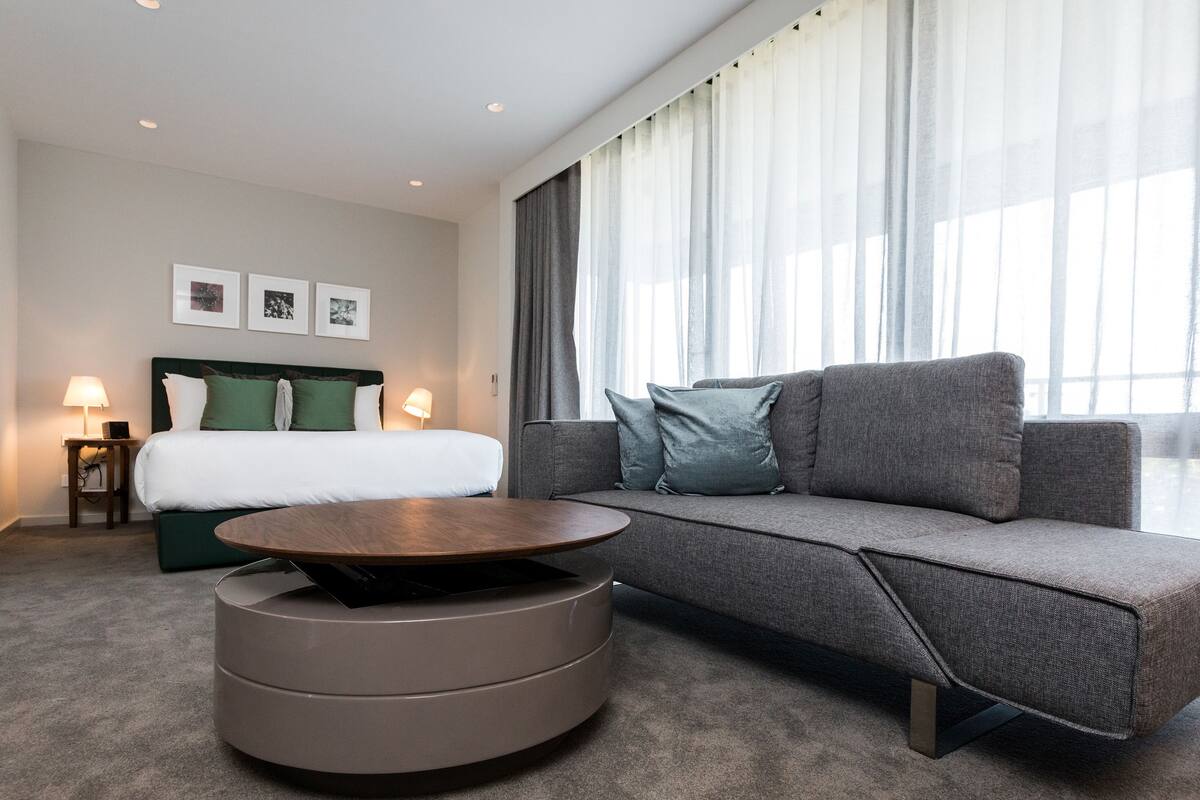A hotel room with a bed, a sofa, a round coffee table, and a window with curtains.