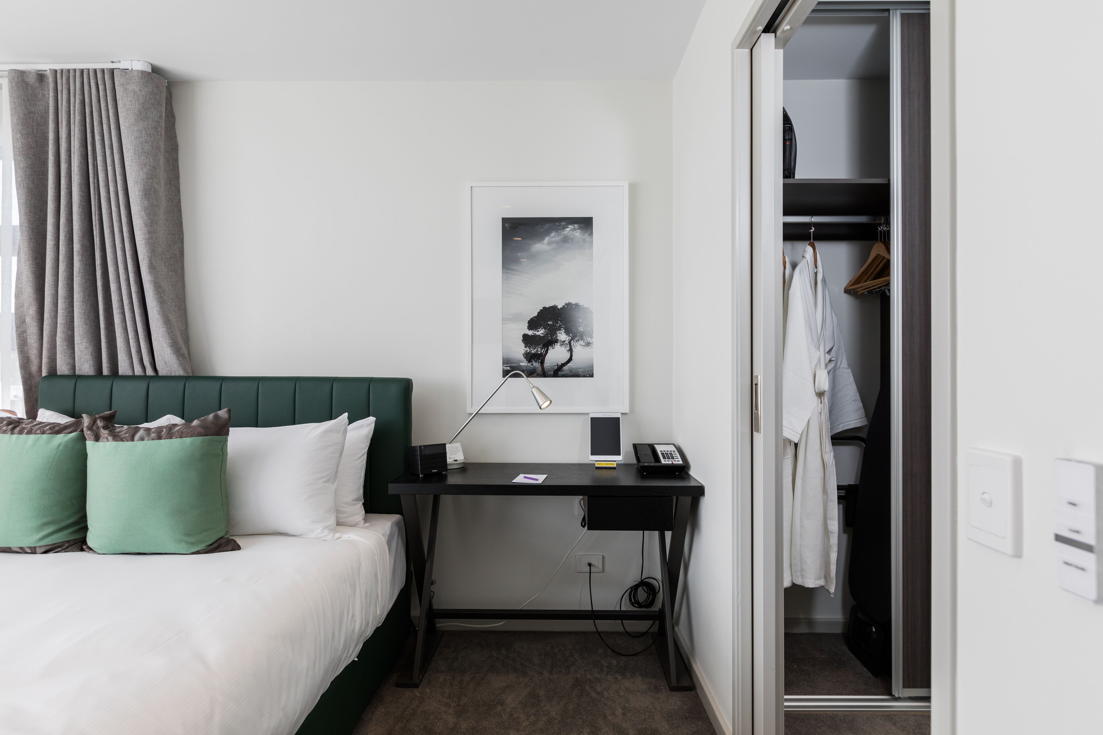 Una habitación de hotel con cama, escritorio, armario y un cuadro en la pared.