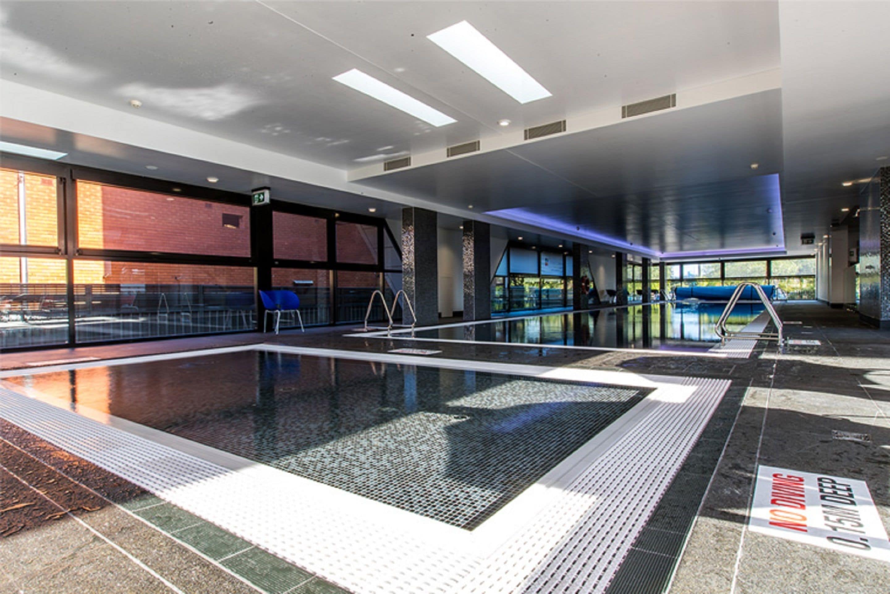 Una piscina interior con carriles claramente delimitados, una silla de salvavidas y un cartel de prohibición de saltos.