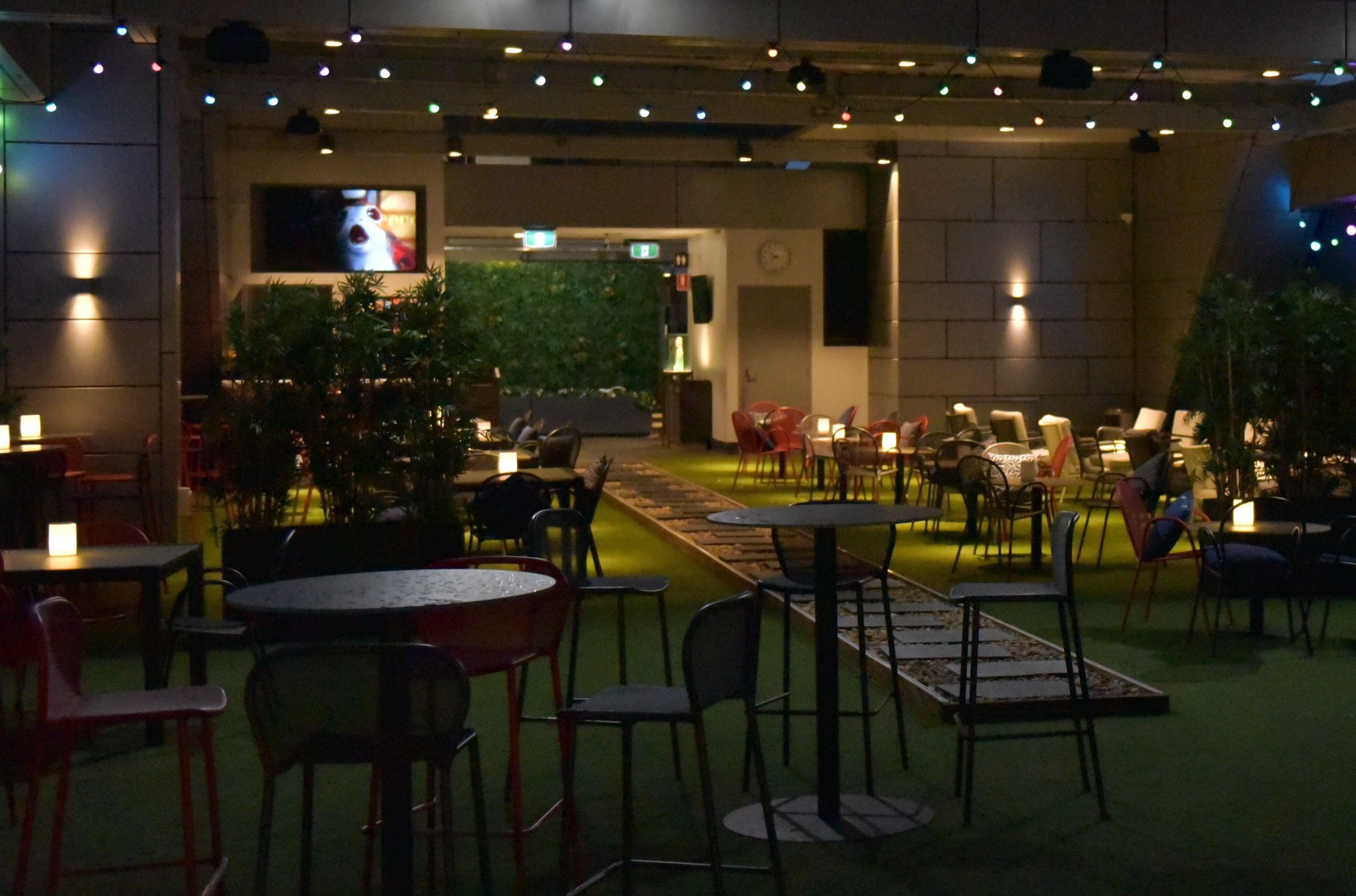 An indoor dining area with tables and chairs, a television screen, and a green wall with plants.