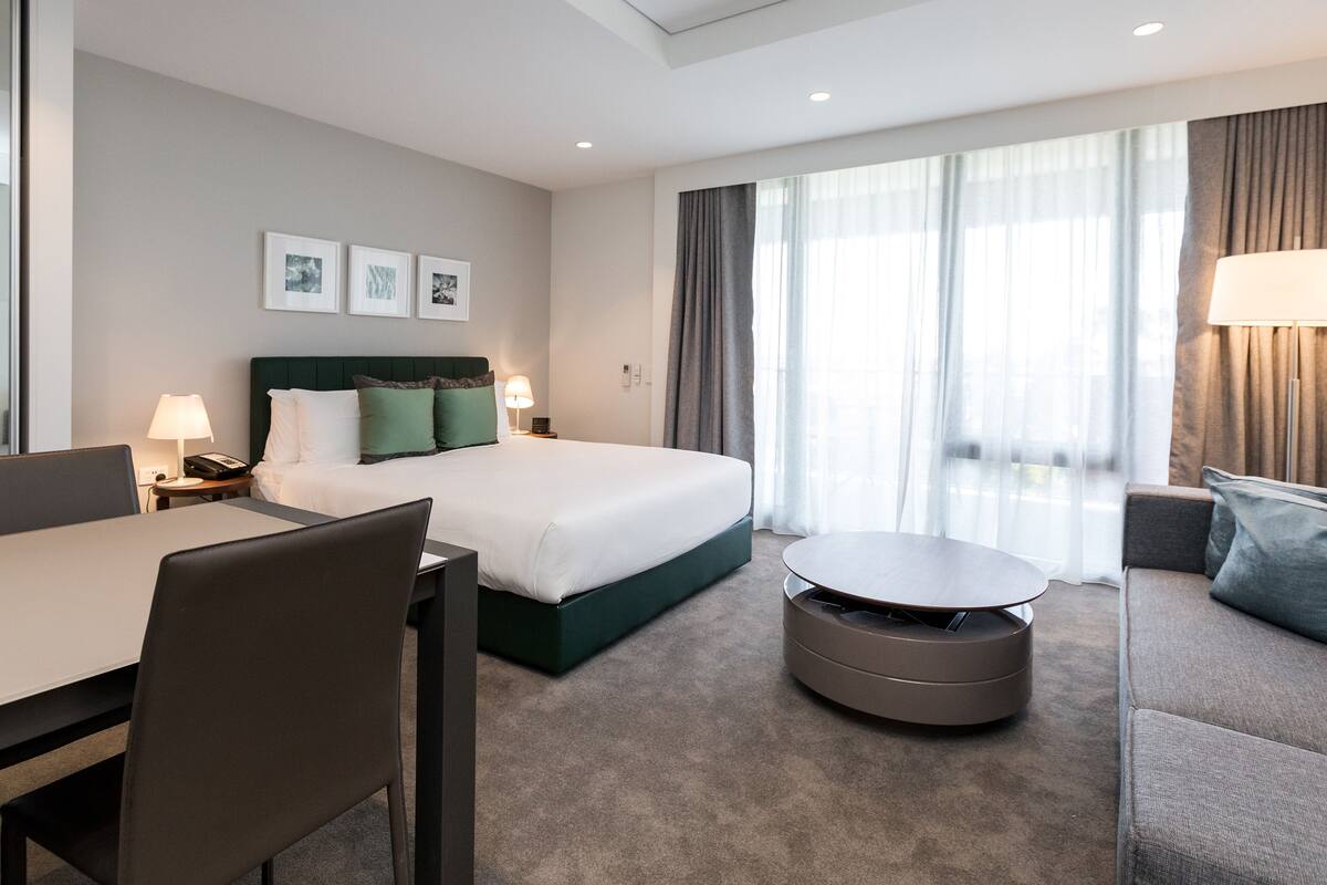 A modern hotel room with a neatly made bed, a dining area, and a sofa.
