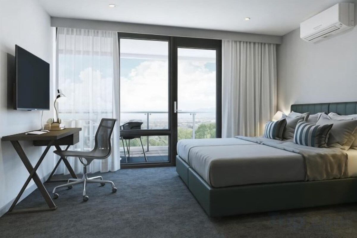 A hotel room with a bed, a desk, a chair, a television, and a balcony with a view.