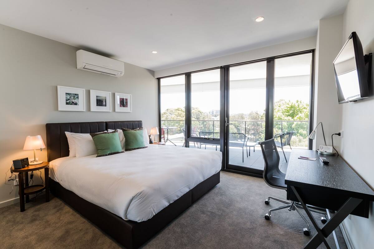 A modern hotel room with a large bed, a desk, and a balcony with a view.