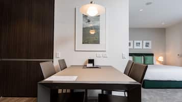 A modern hotel room with a dining area, a bed with green pillows, and a framed picture on the wall.