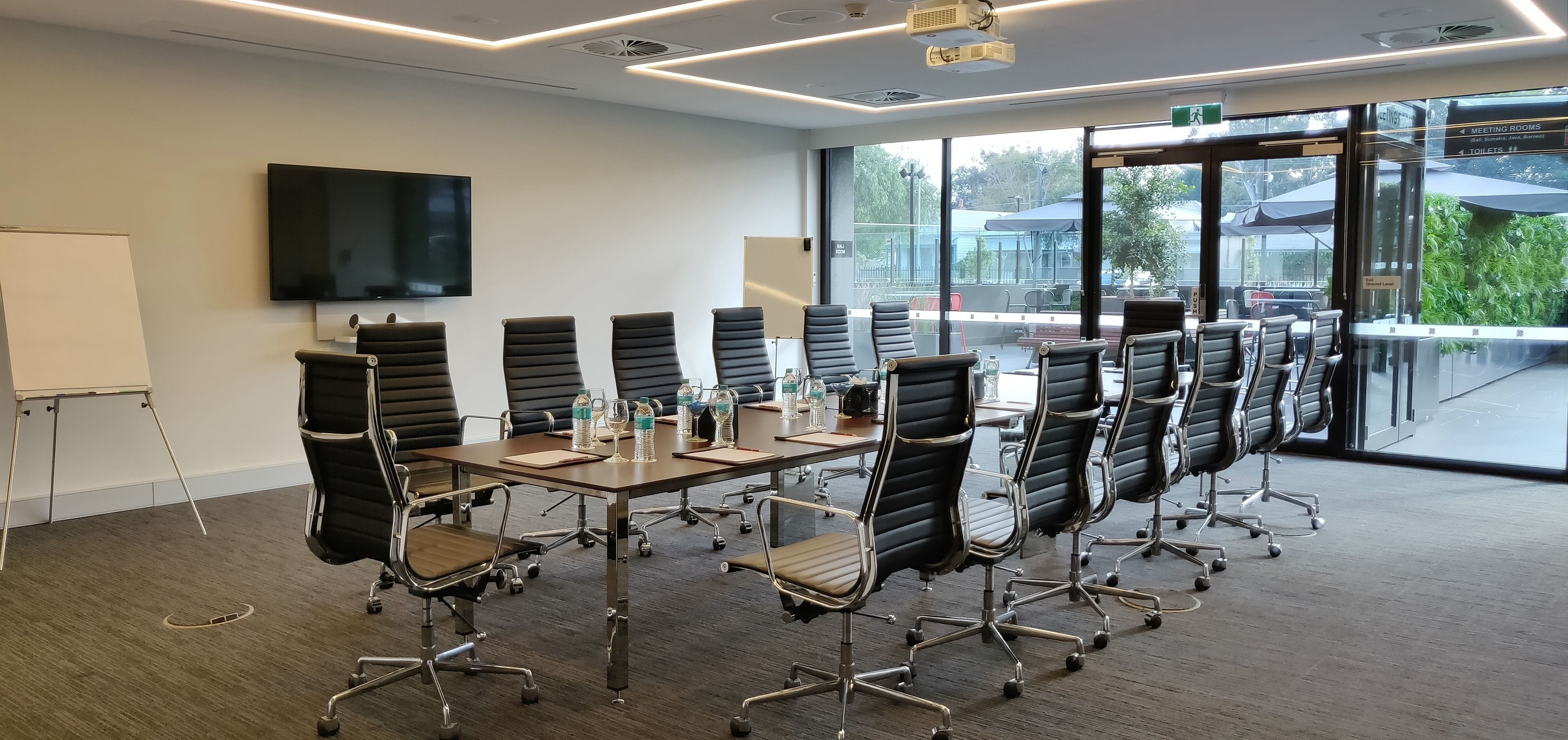 A conference room with a long table, black chairs, a flat-screen TV, and large windows.