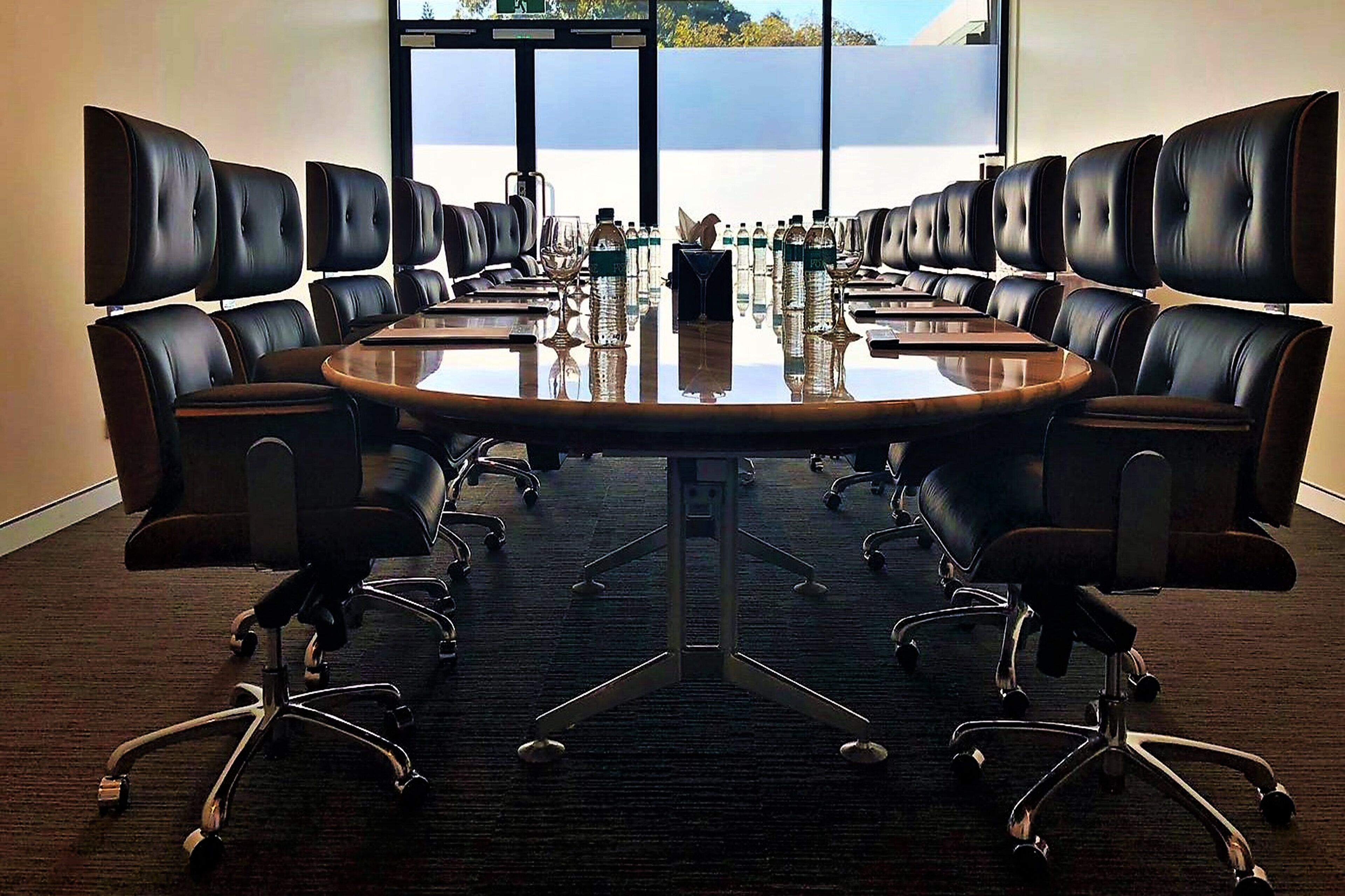 A conference room with a large oval table surrounded by black leather chairs with metal legs.