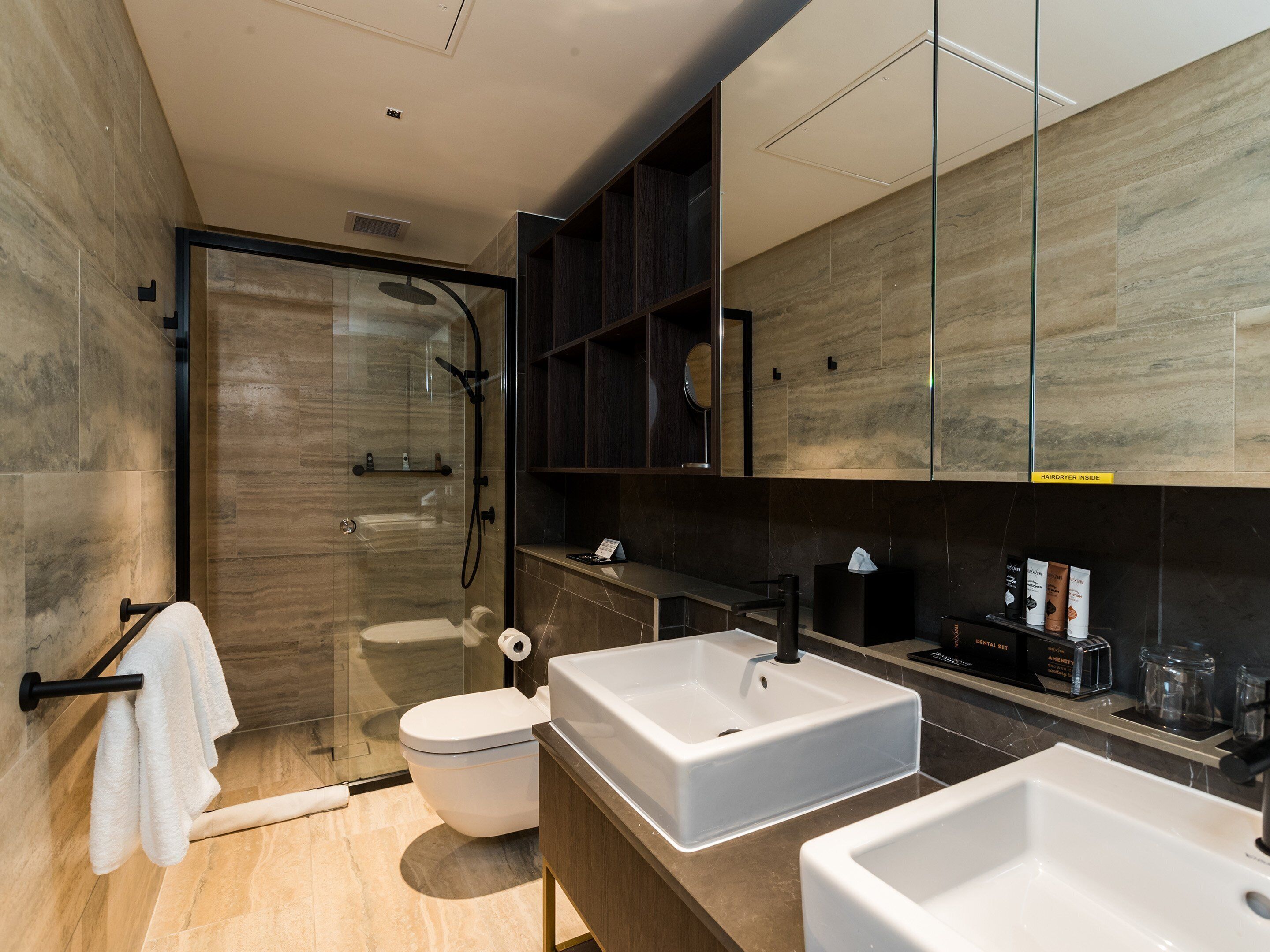 Un baño moderno con ducha de vidrio, inodoro y dos lavamanos.