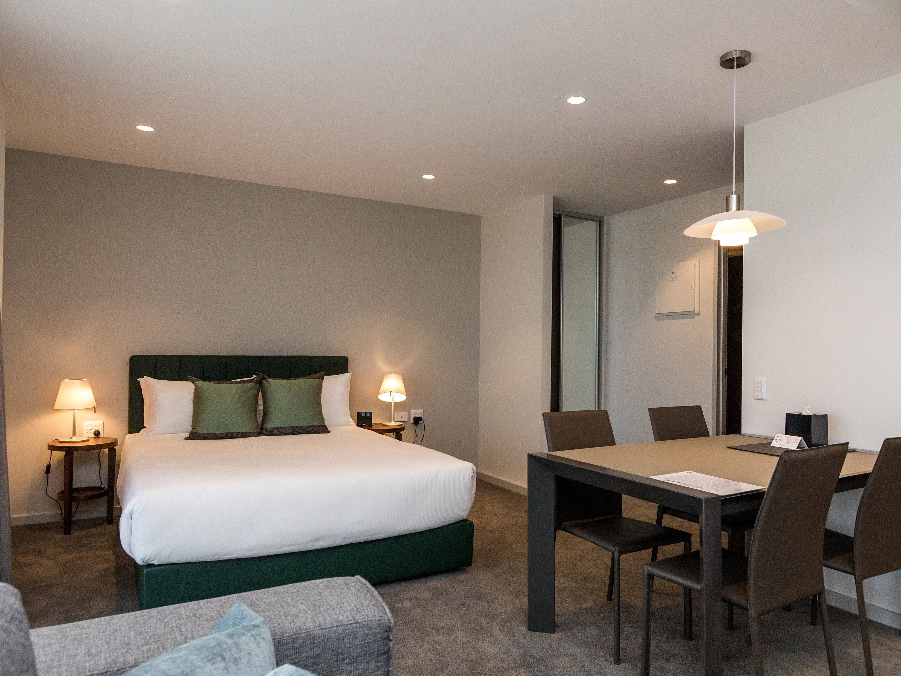 Et hotelværelse med seng, sengeborde, et skrivebord, stole og en hængende lampe.