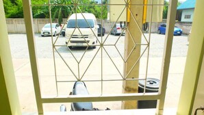 Vista a través de una ventana con rejas, que muestra un estacionamiento con varios coches y un edificio al fondo.