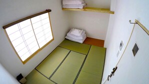 A room with tatami flooring, a shoji screen, a shelf with folded towels, and a small window. - Hiroshima Hostel EN (Hiroshima)