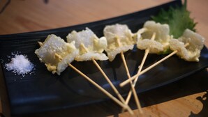 A plate with skewered food items, a leaf garnish, and a small pile of salt. - Hiroshima Hostel EN (Hiroshima)