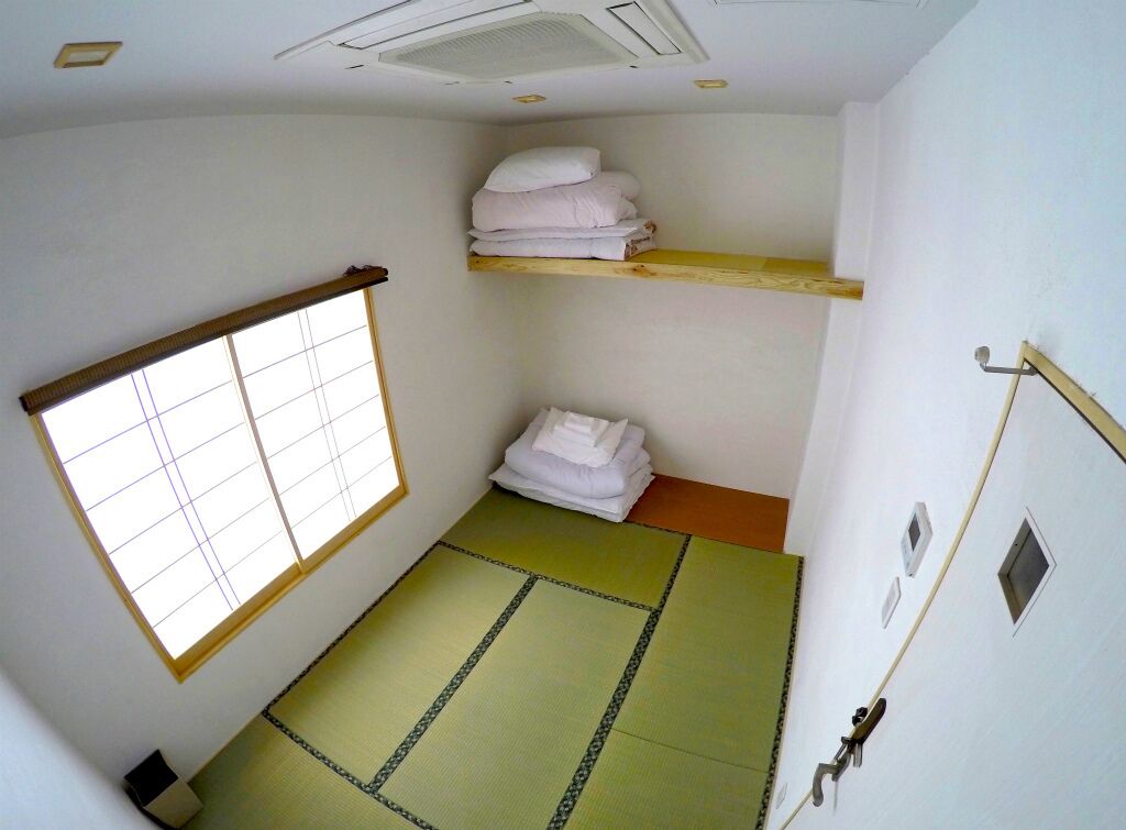 A room with tatami flooring, a shoji screen, a wooden shelf with towels, and a small window.