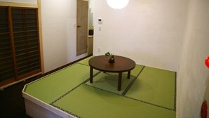 A tatami mat room with a round table, a wooden door, and a hanging light fixture. - Hiroshima Hostel EN (Hiroshima)