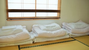 A room with tatami mats, a window with blinds, and neatly folded bedding. - Hiroshima Hostel EN (Hiroshima)