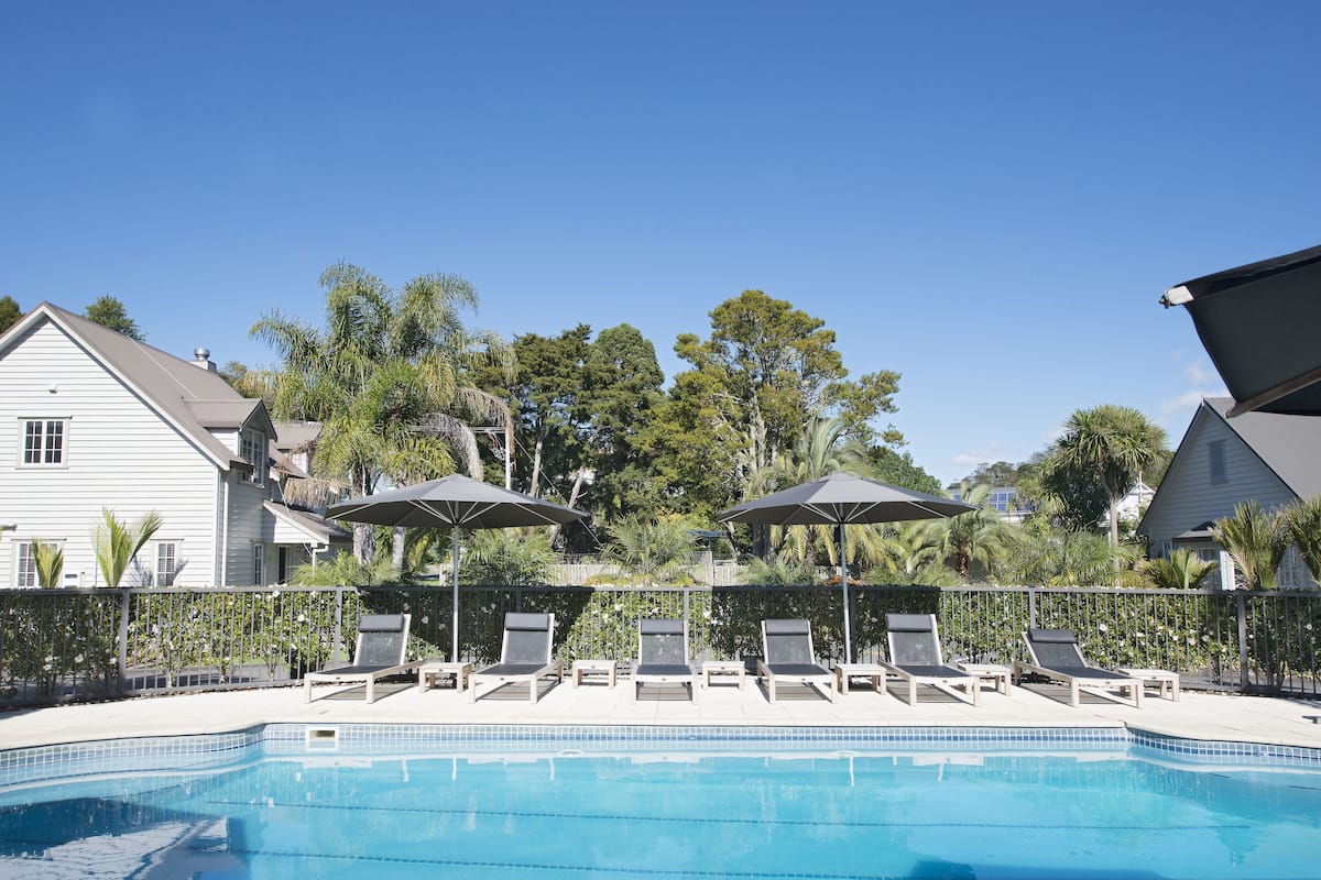 A swimming pool with lounge chairs and umbrellas, surrounded by a fence and trees.