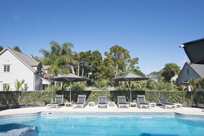 A swimming pool with lounge chairs and umbrellas, surrounded by a fence and trees.