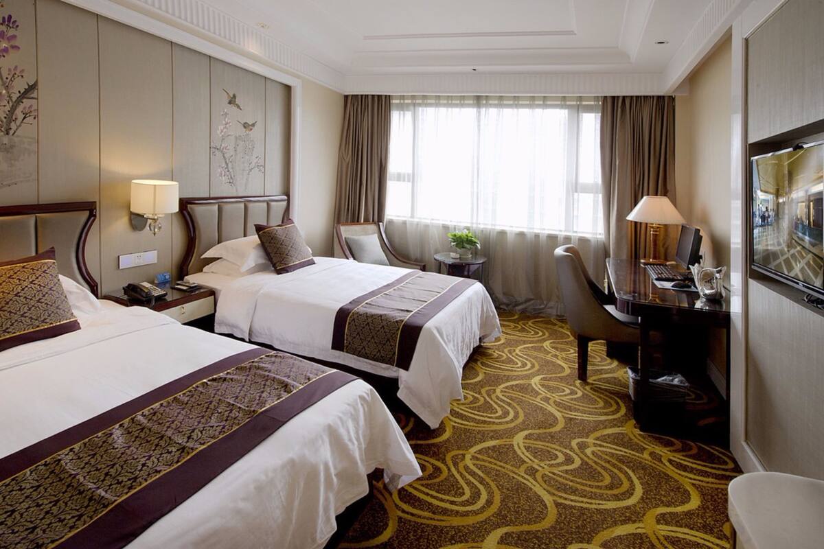 Een hotelkamer met twee bedden, een bureau met een computer, een stoel, een televisie en een raam met gordijnen.