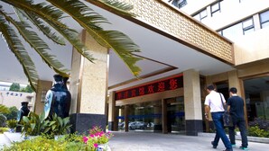 A hotel entrance with a large red sign, palm trees, and potted plants. - HangZhou HuaYang Hotel (Hangzhou)