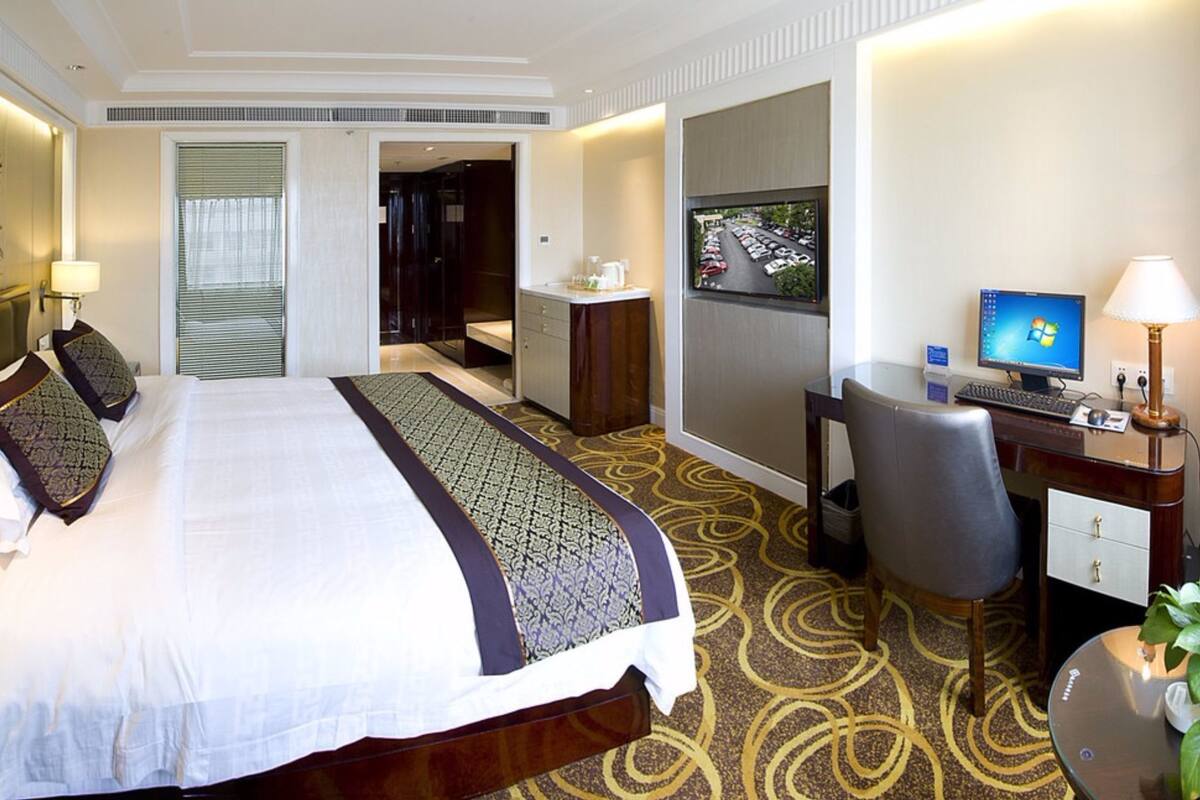 Een hotelkamer met een groot bed, een bureau met een computer, een telefoon en een televisie.
