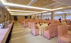 Un salón de banquetes con mesas redondas y sillas, una larga mesa de buffet y un techo decorativo.