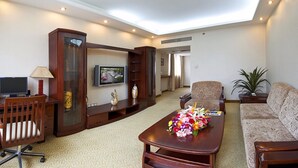 A hotel room with a wooden desk, a television, a sofa, and a decorative vase with flowers. - HangZhou HuaYang Hotel (Hangzhou)