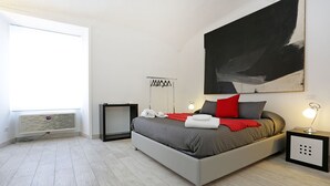 Un dormitorio moderno con una cama gris, almohadas rojas y grises, un cuadro abstracto grande, una lámpara de pie y un radiador.