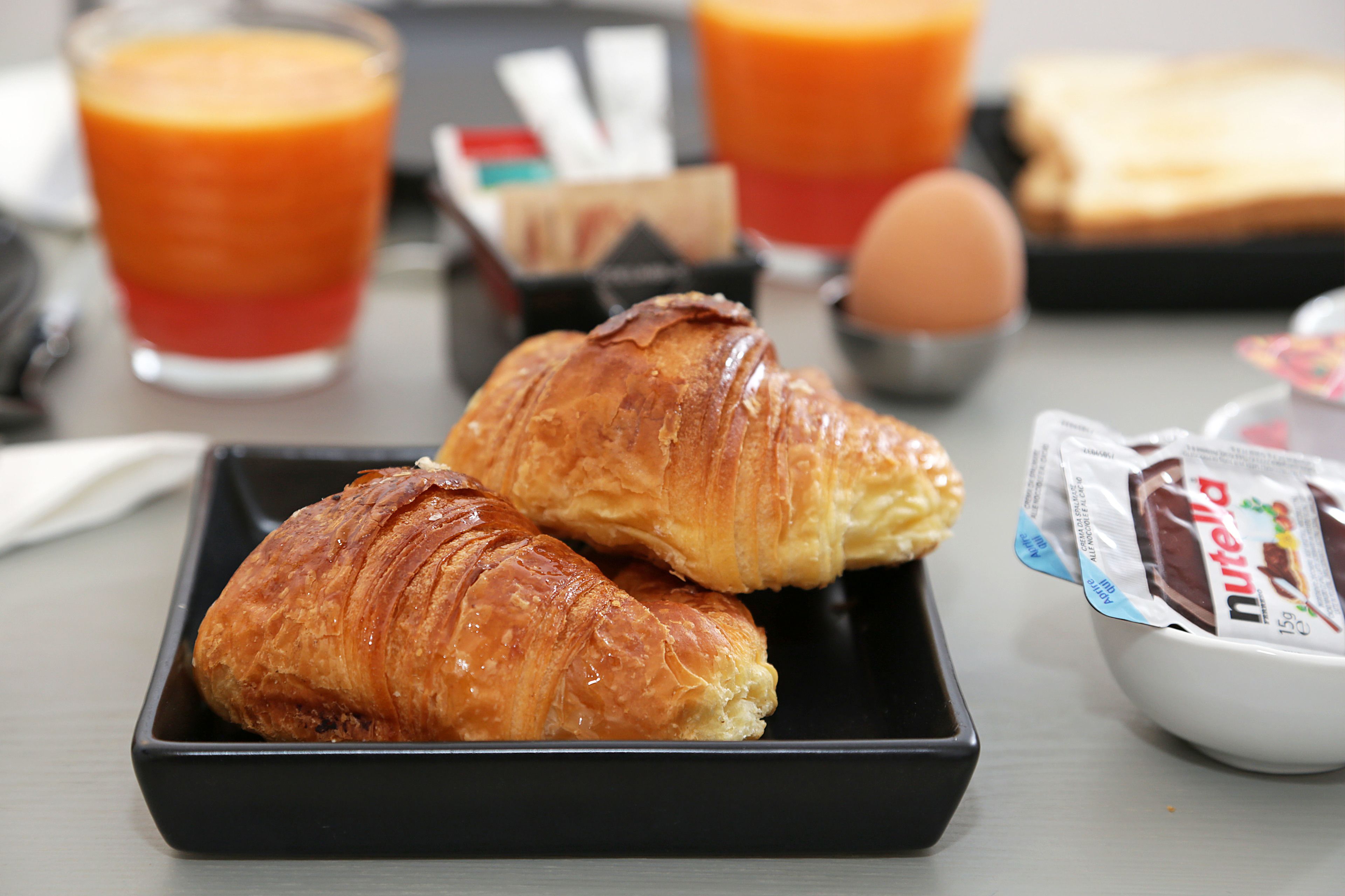 Croissants on a black tray, a glass of orange juice, and a bowl of Nutella.