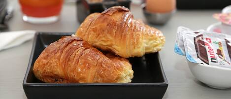 Croissants on a black tray, a glass of orange juice, and a bowl of Nutella.