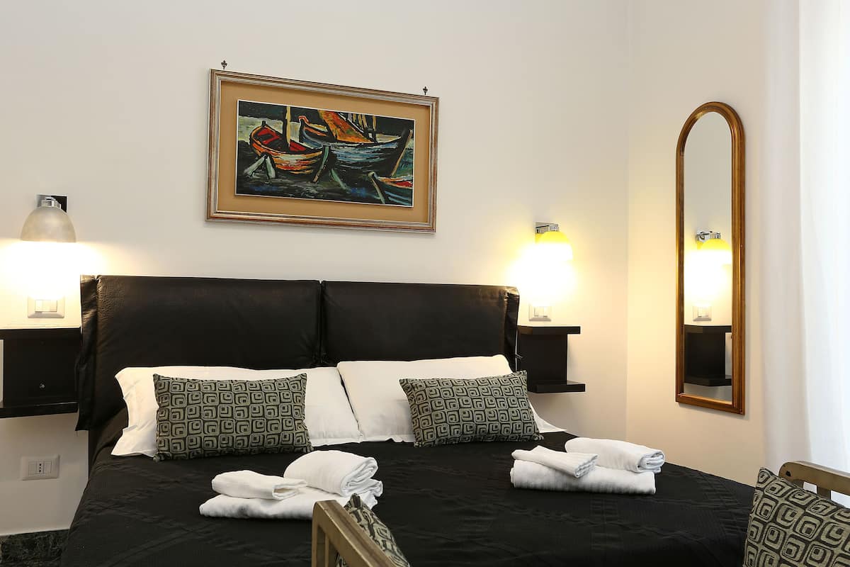 A neatly made bed with pillows, a framed painting above, and a mirror on the wall.