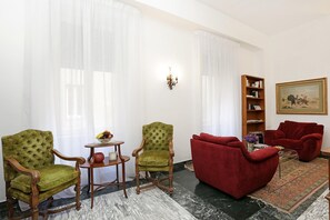 A living room with two green armchairs, a red sofa, a small table with a fruit bowl, and a bookshelf. - Houspitality Caesar B&B (Rome)