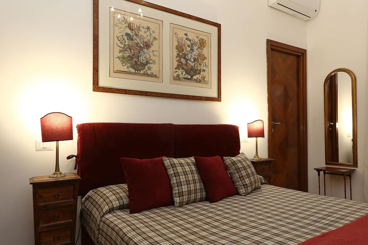 A bedroom with a bed, two bedside tables, a mirror, and two framed botanical prints on the wall.