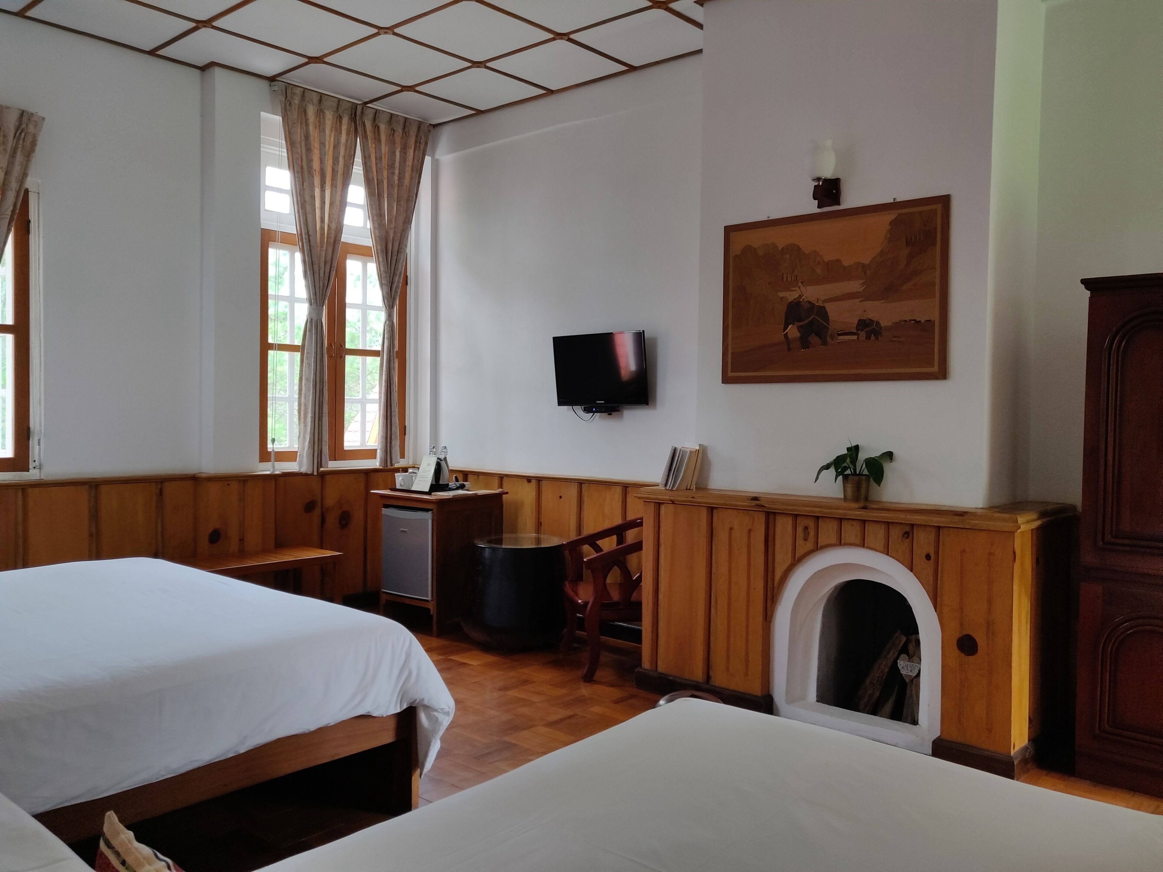 A hotel room with two beds, a television, a fireplace, and a painting on the wall.